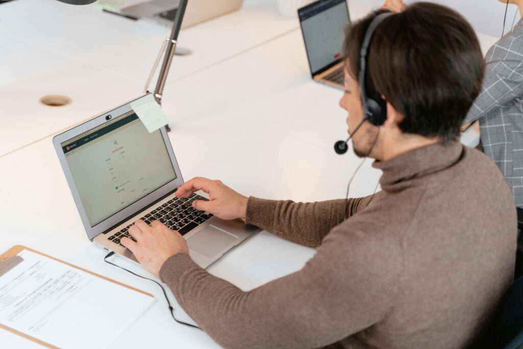 Call center agent wearing headphones working on a laptop in a modern office setting.